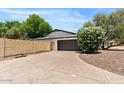 Spacious driveway leading to a two-car garage and large privacy wall, lined with vibrant foliage and trees at 5912 E Wethersfield Rd, Scottsdale, AZ 85254