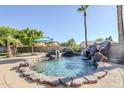 Backyard swimming pool with rock waterfall feature and lush landscaping with clear blue sky at 12434 S Ki Cir, Phoenix, AZ 85044