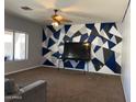 Open living room with ceiling fan, large window, and wall with painted geometric shapes at 43418 W Wild Horse Trl, Maricopa, AZ 85138