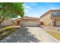 Single-story home featuring a two-car garage, desert landscaping, and a mature tree shading the driveway at 817 E Lamonte St, San Tan Valley, AZ 85140
