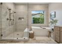 Bright bathroom featuring a glass-enclosed shower, soaking tub beneath a window, and neutral stone tile throughout at 4350 S White Dr, Chandler, AZ 85249