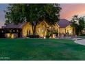 A well-manicured front yard and home featuring a stone facade and mature shade tree at dusk at 2558 E Page Ct, Gilbert, AZ 85234
