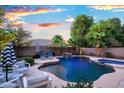 Inviting swimming pool and spa with a rock waterfall feature and outdoor seating area with umbrellas and mature landscaping at 2056 E Carob Dr, Chandler, AZ 85286