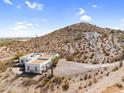 Wide aerial shot of a modern home nestled against a hillside with desert scenery and clear blue sky at 1550 W Adobe Dam Dr, San Tan Valley, AZ 85144