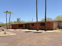 Exterior shot of a single-story brick house with palm trees, desert landscaping, and a gravel driveway at 11041 N Hayden Rd, Scottsdale, AZ 85260