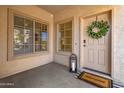 Inviting front porch with a charming welcome mat, a decorative lantern, a wreath and sunlit windows at 15046 W Post Dr, Surprise, AZ 85374