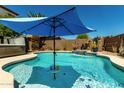 Enjoy the shimmering blue waters of this private pool with an umbrella, waterfall, and desert landscaping at 861 E Indian Wells Pl, Chandler, AZ 85249