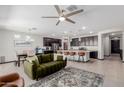 Open concept living area featuring a stylish couch, ceiling fan, kitchen island with seating, and dining area at 15276 W Latham St, Goodyear, AZ 85338