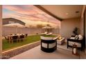 Beautiful backyard featuring green grass, dining table, a fire pit, and lounge chairs under sun umbrellas at 17652 W Fetlock Trl, Surprise, AZ 85387