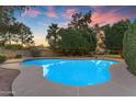 An inviting backyard pool glistening under a colorful dusk sky, surrounded by lush greenery for ultimate privacy at 8604 S Oak St, Tempe, AZ 85284
