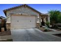 A well-lit garage door is featured in this exterior view of this one story, desert home, with xeriscaping at 14360 W Pershing St, Surprise, AZ 85379