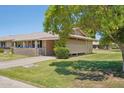 Spacious lawn area, mature tree, and home exterior view with covered carport at 10431 W Roundelay Cir, Sun City, AZ 85351