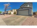 Two-story home with a two-car garage, neutral tones, desert landscaping, and mature trees at 12325 W Dreyfus Dr, El Mirage, AZ 85335