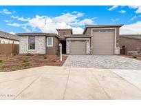 Charming single-story home with a stone accent facade, a brick driveway, and a two-car garage at 20254 W Hollyhock St, Buckeye, AZ 85396