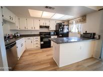 Bright kitchen featuring white cabinets, wood floors, black appliances, and a countertop bar at 6337 N 49Th Ave, Glendale, AZ 85301