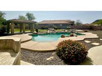 Backyard pool with rock waterfall feature, beautiful landscaping, and covered patio area at 9827 W Keyser Dr, Peoria, AZ 85383