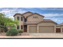 Tan two-story home with a three car garage, tile roof, desert landscaping, and secure window coverings at 43594 W Bravo Ct, Maricopa, AZ 85138