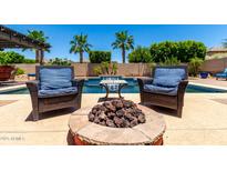 Inviting backyard oasis with a fire pit and comfortable seating by the refreshing pool and lush palm trees at 18174 W Wind Song Ave, Goodyear, AZ 85338