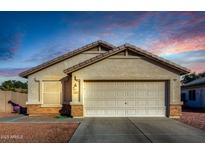 Tan house with a two-car garage and landscaping; sunset in the background at 12962 W Catalina Dr, Avondale, AZ 85392