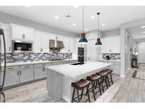 Modern kitchen featuring a large island, white cabinets, stylish backsplash, stainless steel appliances, and wood-look flooring at 20363 W Coolidge St, Buckeye, AZ 85396