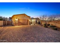 Evening view of home's exterior, showcasing a brick driveway and landscaping at 9825 W Desert Elm Ln, Peoria, AZ 85383