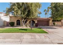 Tan stucco house with brown garage door, lush lawn, and mature trees at 10473 N 87Th Pl, Scottsdale, AZ 85258