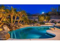 Stunning nighttime view of a luxurious pool with waterfall feature and mountain backdrop at 10756 E Ludlow Dr, Scottsdale, AZ 85255