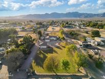 Aerial view of a single story home with a large grassy yard, mountain views, and mature trees at 18335 W Orangewood Ave, Waddell, AZ 85355