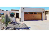 Spanish style home with landscaped front yard, featuring a wooden garage door and desert plants at 18658 E Mazatzal Cir, Rio Verde, AZ 85263