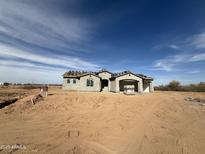 Under-construction home with an open garage in a rural setting, set against a clear blue sky at 21916 W Duane Ln, Wittmann, AZ 85361