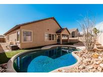 Backyard oasis with a refreshing pool, artificial grass, and rock landscaping at 13550 W Port Au Prince Ln, Surprise, AZ 85379