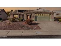 Tan one-story house with solar panels, a green garage door, and nicely landscaped yard at 14846 W Tomahawk Way, Sun City West, AZ 85375