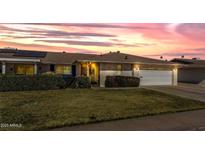 Charming brick home showcasing manicured lawn, solar panels, and an attached two-car garage at sunset at 10850 W Venturi Dr, Sun City, AZ 85351