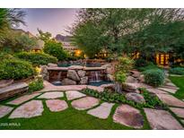Tranquil backyard pool with rock waterfall feature, lush landscaping, and stone walkway to main house at 5747 E Mockingbird Ln, Paradise Valley, AZ 85253