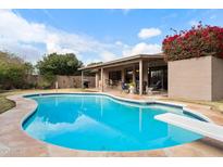 Inviting kidney-shaped pool with diving board, surrounded by a patio and lush landscaping at 9041 E Ludlow Dr, Scottsdale, AZ 85260