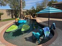 Inviting backyard pool area features playful floats, a waterfall feature, and a comfortable lounge chair with an umbrella at 21362 E Puesta Del Sol Rd, Queen Creek, AZ 85142