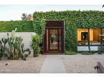 Exterior of the house featuring a decorative steel entrance, desert landscaping, and lush greenery at 6529 E Camino De Los Ranchos St, Scottsdale, AZ 85254