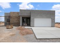 A modern home with a stone accent wall and fresh concrete driveway awaits landscaping at 28583 N 257Th Dr, Wittmann, AZ 85361