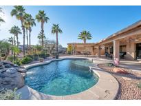 Inviting kidney-shaped pool with a rock waterfall feature, surrounded by a desert landscape at 15973 W Sheila Ln, Goodyear, AZ 85395