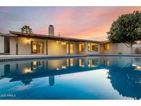 Backyard pool reflecting the house at dusk with a covered patio and lush foliage at 302 E Coral Gables Dr, Phoenix, AZ 85022