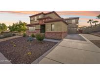 Two-story home featuring desert landscaping, red stone accents, and a long driveway at 12017 W Monte Lindo Ln, Sun City, AZ 85373