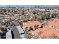 Aerial view of residential community, featuring red tile roofs, covered parking, landscaping, and city skyline in background at 1905 E University Dr # 216, Tempe, AZ 85288