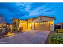 Charming home with a paver driveway and three-car garage, enhanced by warm exterior lighting and stone accents at 10254 W Bent Tree Dr, Peoria, AZ 85383