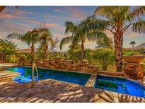 Beautiful blue swimming pool with integrated spa, stone waterfall feature, and lush tropical landscaping at 1681 E Maygrass Ln, Queen Creek, AZ 85140