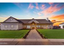 Beautifully designed home with a covered porch, complemented by lush green lawn and colorful sunset at 2312 N Raven --, Mesa, AZ 85207