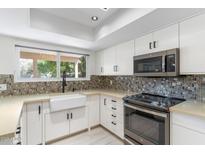 Modern kitchen featuring white cabinets, mosaic backsplash, stainless steel appliances, and a farmhouse sink under the window at 4220 E Everett Dr, Phoenix, AZ 85032