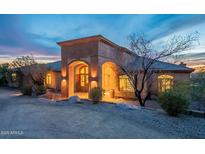 Stunning exterior shot of a home with unique architectural features, beautiful desert landscaping, and warm lighting at dusk at 3086 N Herrala Way, Apache Junction, AZ 85119