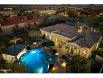 Aerial view of a private pool and spa with a covered bar area and fire pit at dusk at 37080 N 109Th Way, Scottsdale, AZ 85262