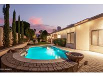 Inviting backyard pool with lush landscaping, ambient lighting, and a serene twilight sky at 16428 N 59Th St, Scottsdale, AZ 85254