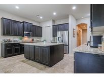 Well-lit kitchen featuring an island with a sink, stainless steel appliances, and dark wood cabinets at 2320 E Allen St, Phoenix, AZ 85042